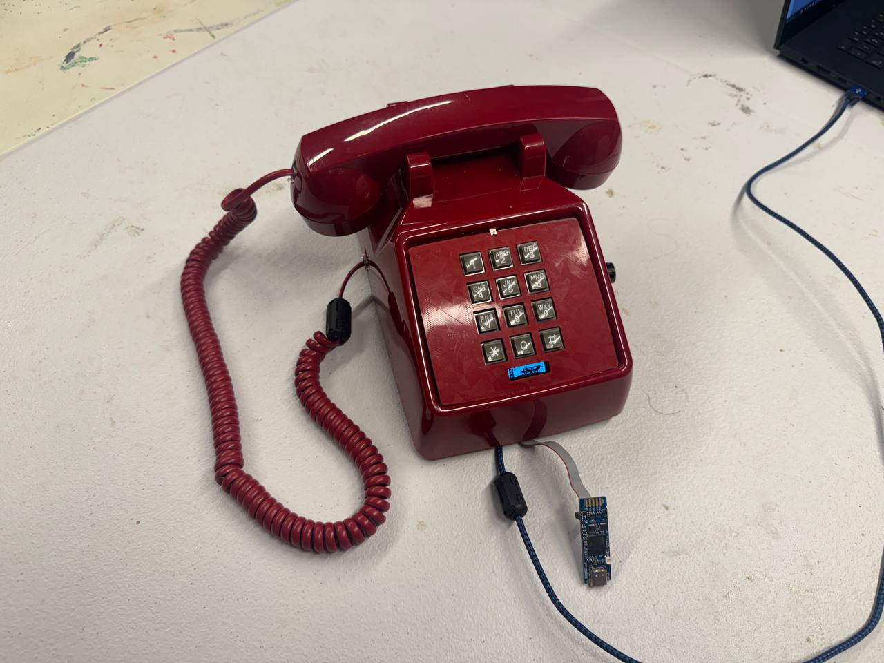 A burgundy push-button telephone modified with an OLED and exposed electronics